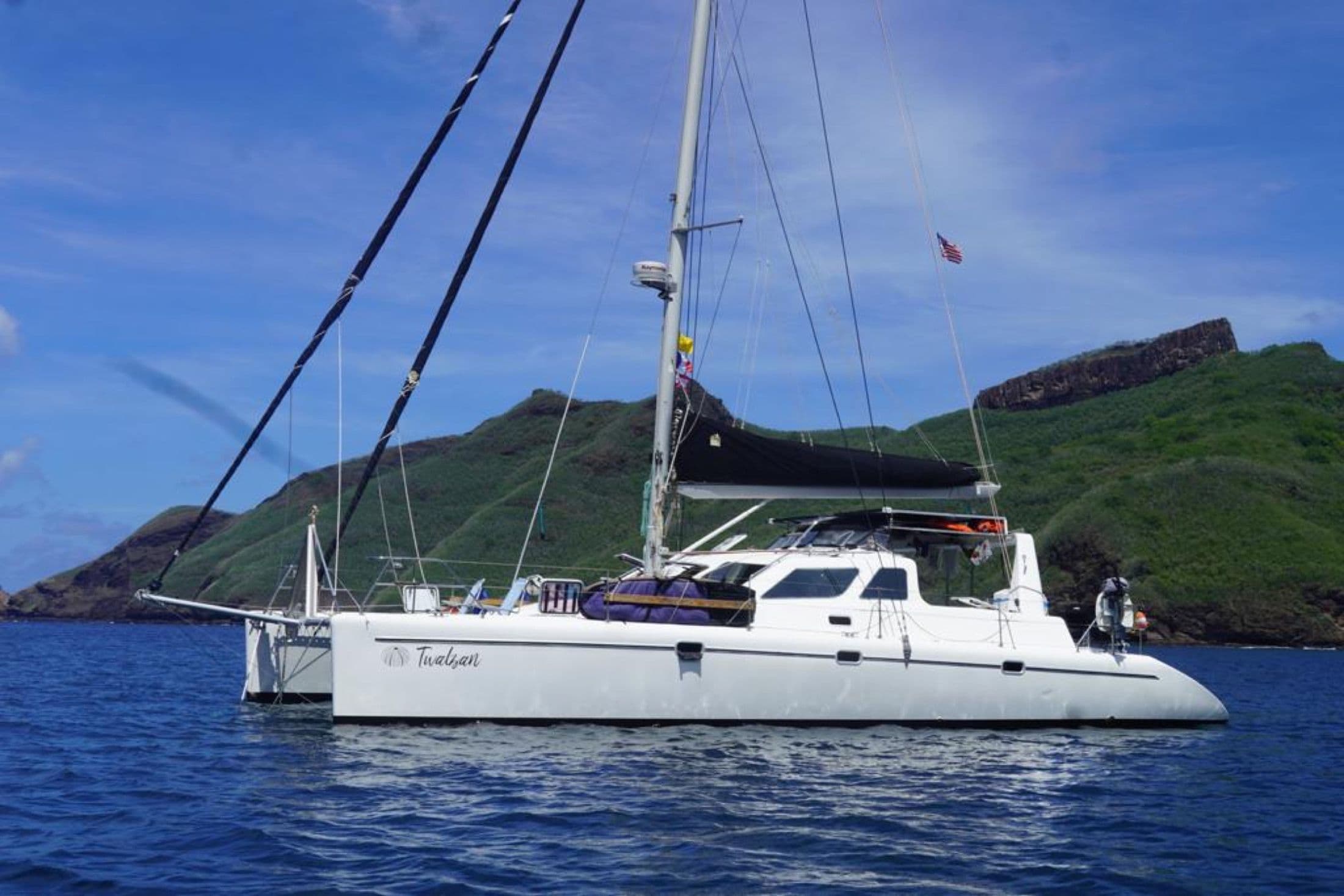 A catamaran at anchor in blue water beneath a volcanic island